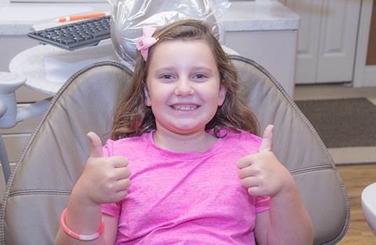 Young girl in dental chair giving two thumbs up