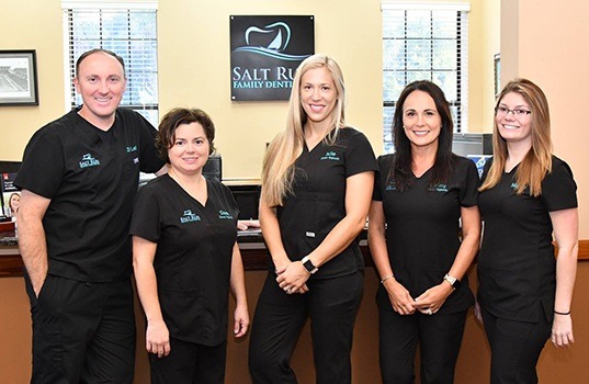 Dental team members smiling together in front of reception desk