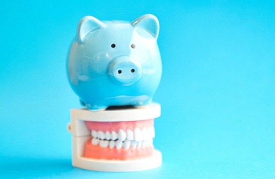Piggy bank atop model teeth representing cost of cosmetic dentistry St. Augustine 