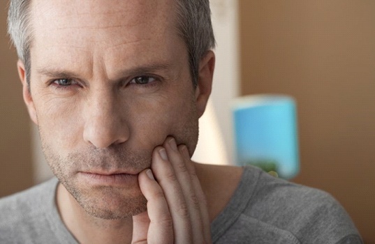 gray-haired man holding his mouth in pain