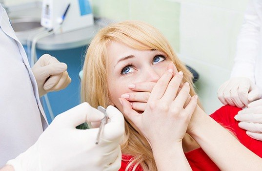 Fearful patient in need of sedation dentistry covering mouth in dental chair