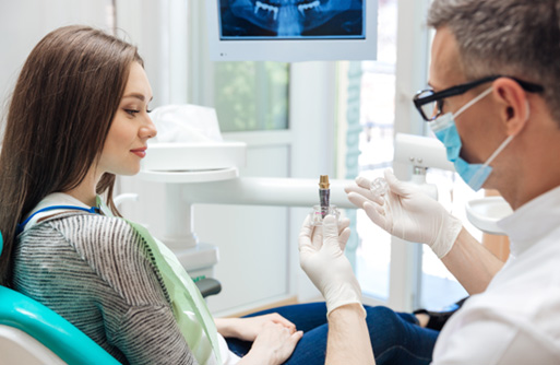 Dentist showing patient in dental chair a sample implant