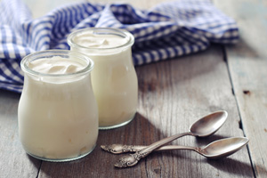 Two glass jars of yogurt with spoons on wooden surface