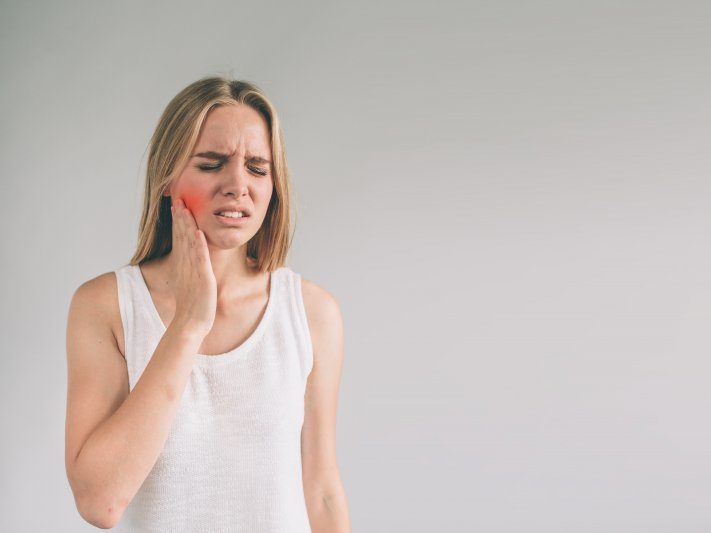 person with tooth pain holding their cheek