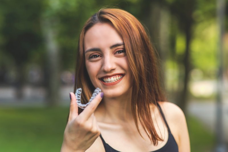 Red-haired woman outside holding Invisalign aligner