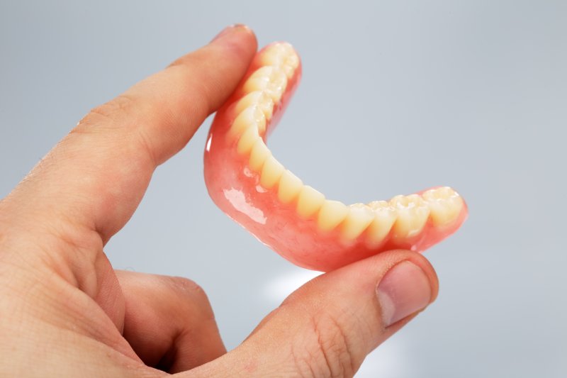 A hand holding loose lower dentures