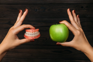 Left hand holding a set of dentures and right hand holding a green apple