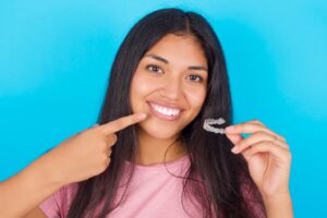 Teenage girl holding clear aligner and pointing to smile.